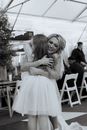 A joyful moment captured at a wedding reception under a white tent with folding chairs in the background.