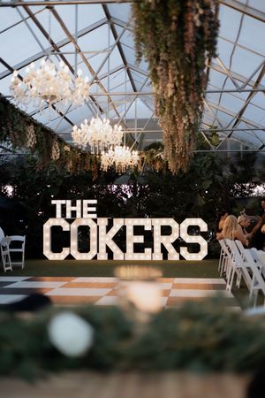 A wedding venue with crystal chandeliers and hanging greenery featuring large illuminated 'THE COKERS' signage.