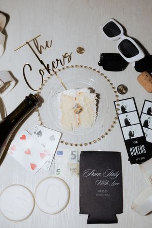 Overhead view of party supplies including sunglasses, playing cards, drink koozies and photo booth strips on a white surface.
