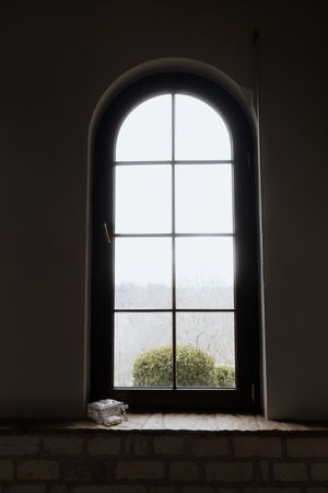 Arched window with divided panes in a stone wall letting in natural light against a dark interior.