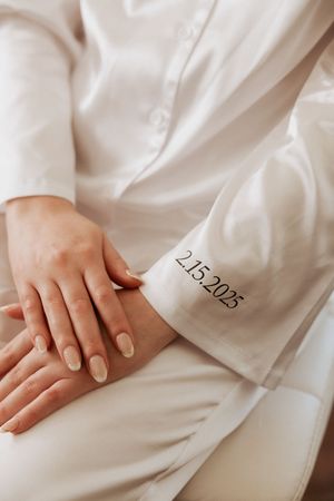 Close-up of hands showing embroidered wedding date 2.15.2025 on white bridal attire sleeve.