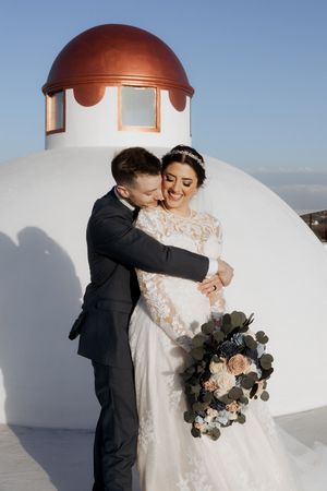 A romantic moment between newlyweds against a white domed building with a beautiful floral bouquet.