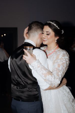 Tender wedding reception moment captured in low light with elegant lace dress details.
