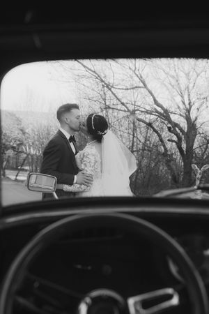 Black and white view through car window of couple's romantic moment on their wedding day.
