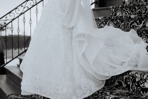 A white bridal gown with an ornate lace train and corset bodice hangs against an ornamental iron railing.