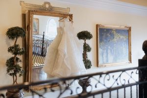 An elegant staircase railing curves up the stairs with a wedding dress and decorative topiaries visible in the background.