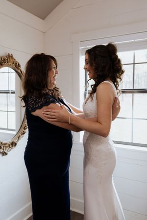 Two women sharing an emotional moment in a white room with an ornate gold mirror.