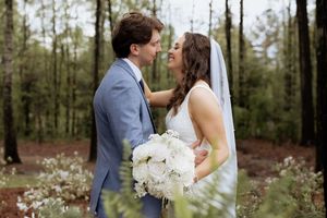 Romantic wedding portrait of couple with white bouquet in a forest setting.
