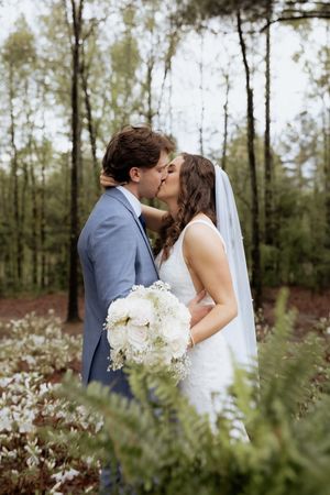 Romantic wedding couple shares intimate moments among trees in a wooded setting.