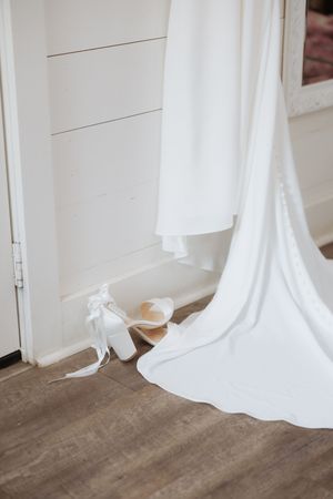 White wedding dress train and shoes against a light colored wooden floor and wall.