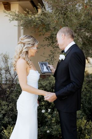 Bride and groom sharing an emotional first look moment while holding a framed photo outdoors.