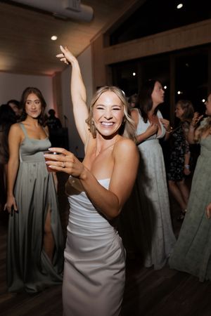 Joyful bride in white gown dancing with arm raised at wedding reception.