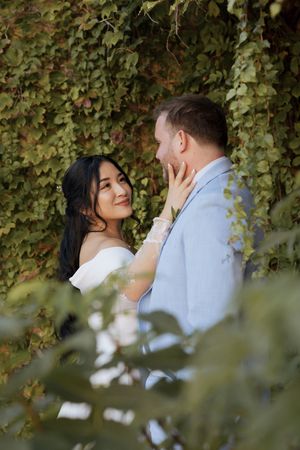 Bride tenderly touching grooms face surrounded by lush green ivy at outdoor wedding.