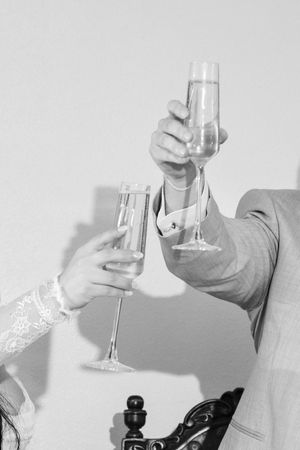 Black and white photo of bride and groom toasting with champagne flutes at their wedding reception.