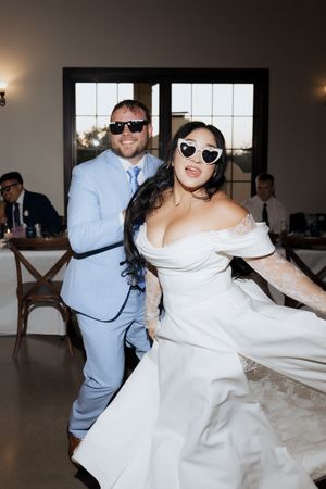 Bride and groom dancing in heart sunglasses during fun wedding reception celebration.
