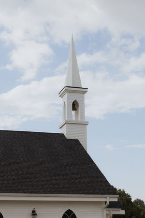 White church steeple with bell tower against a partly cloudy blue sky.