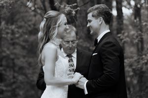 Black and white photo of bride and groom exchanging vows with officiant outdoors.