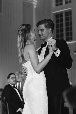 Bride and groom share first dance in black and white wedding reception photo.