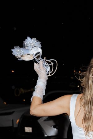 Woman in white dress and lace gloves holding decorative masquerade masks at night.