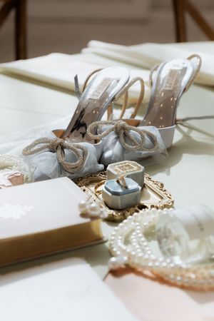 Elegant bridal accessories including crystal bow heels, pearl necklace, and ring box on display.