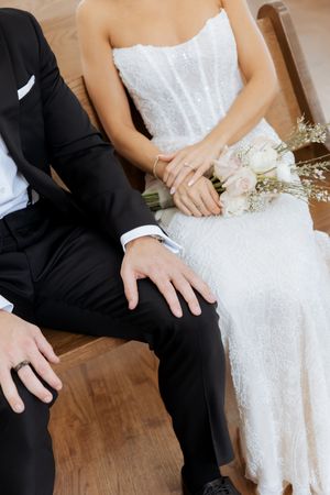 Close-up of bride and groom holding hands with a white rose bouquet during their wedding ceremony.