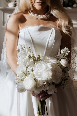 A bridal bouquet of elegant white roses and flowers held against a classic white wedding dress.