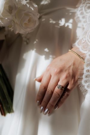Close-up of bridal hands showing engagement ring and lace dress details.
