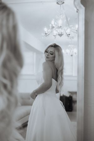 Ethereal bridal portrait with flowing white gown under crystal chandelier in soft natural light.