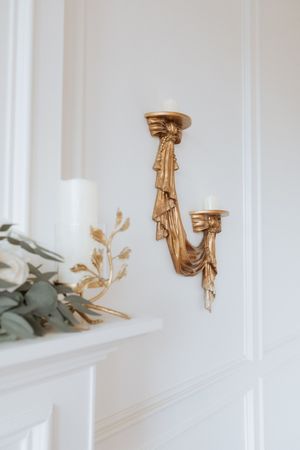 Gold decorative wall sconces and floral accents adorn a white paneled wall in an elegant interior space.
