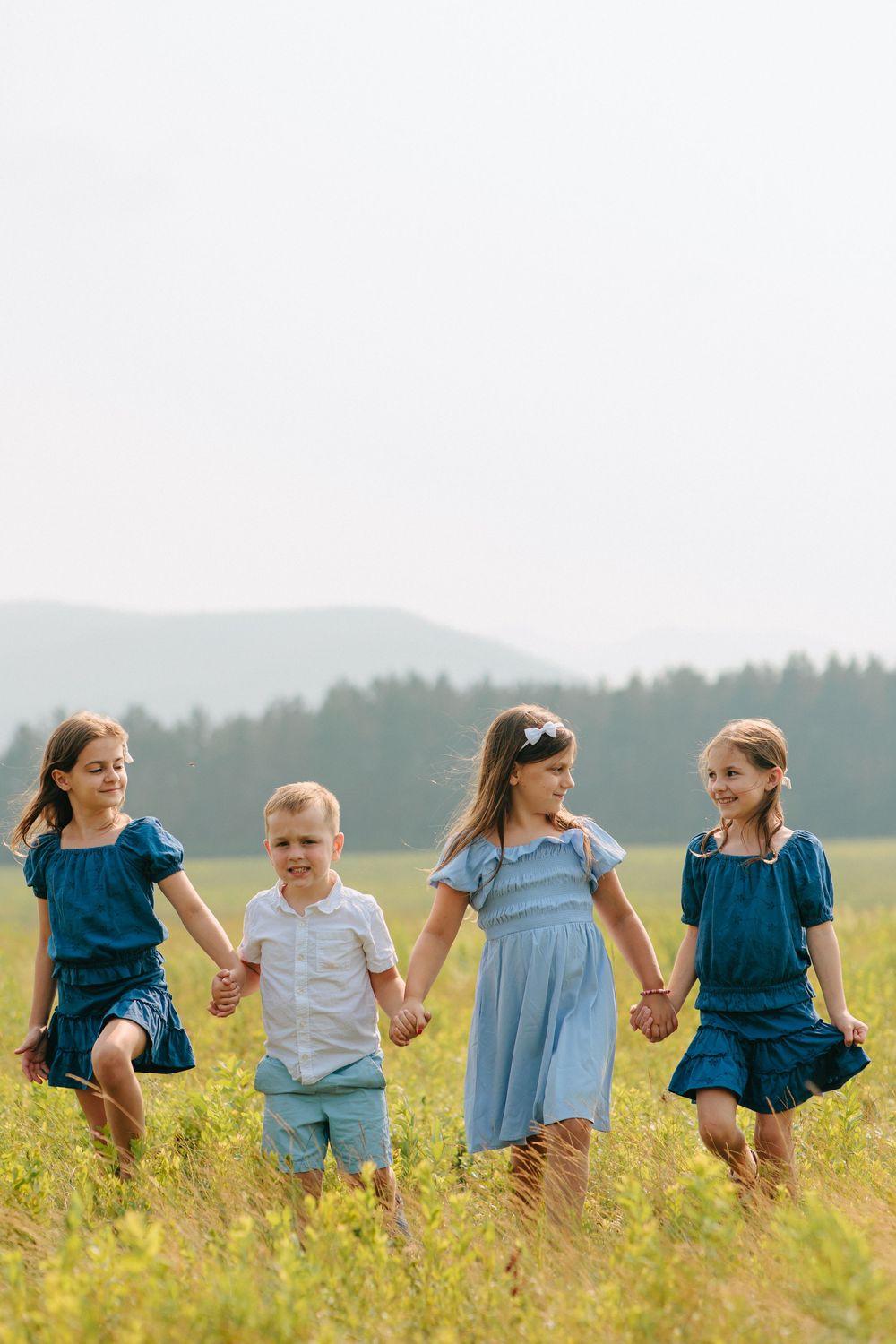 Children holding hands while walking through a field of tall yellow flowers on a bright summer day.