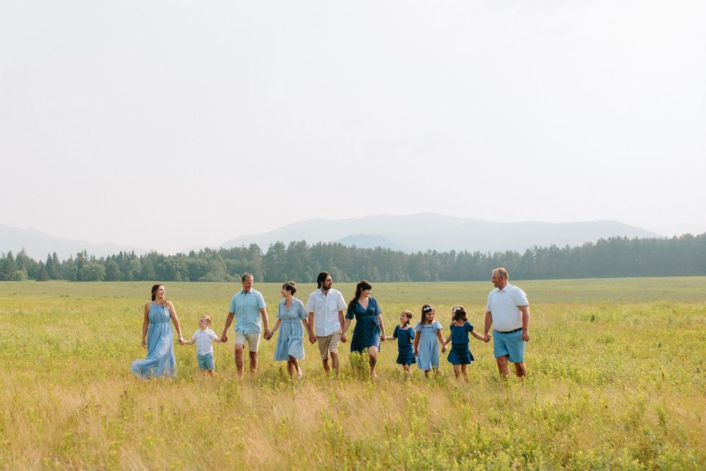 A group of people in blue and white outfits walking together through a sunny meadow with trees in the background.