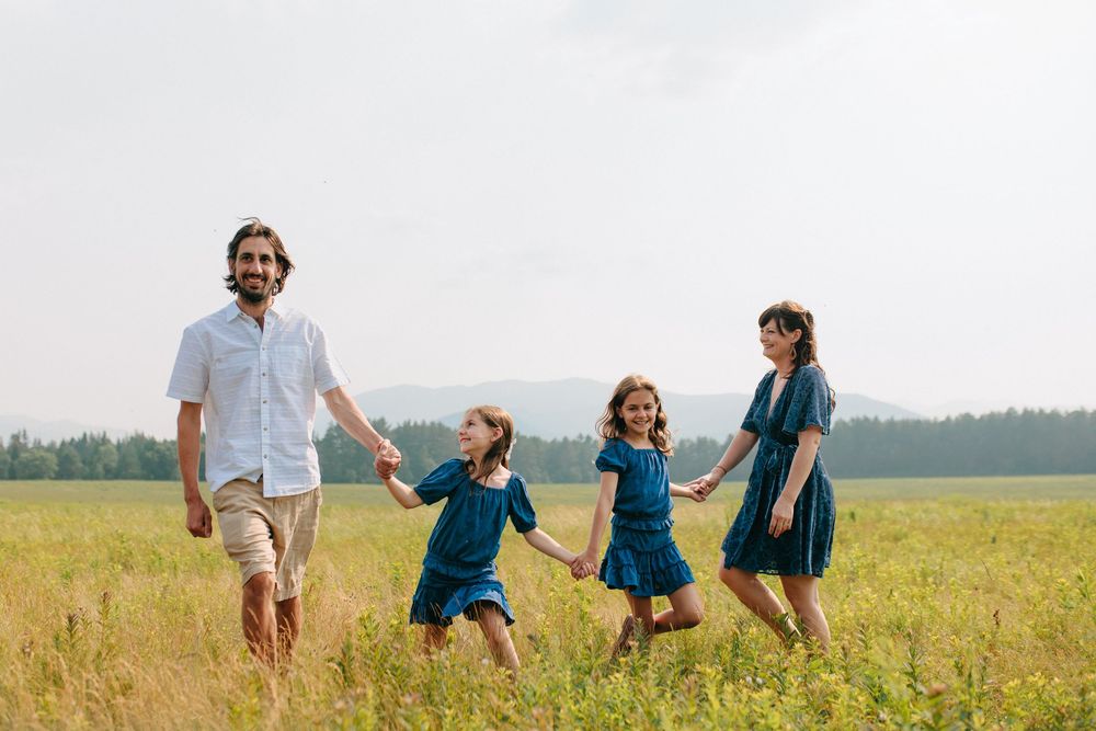 People enjoying a sunny day while walking through a golden field with forest views in the distance.