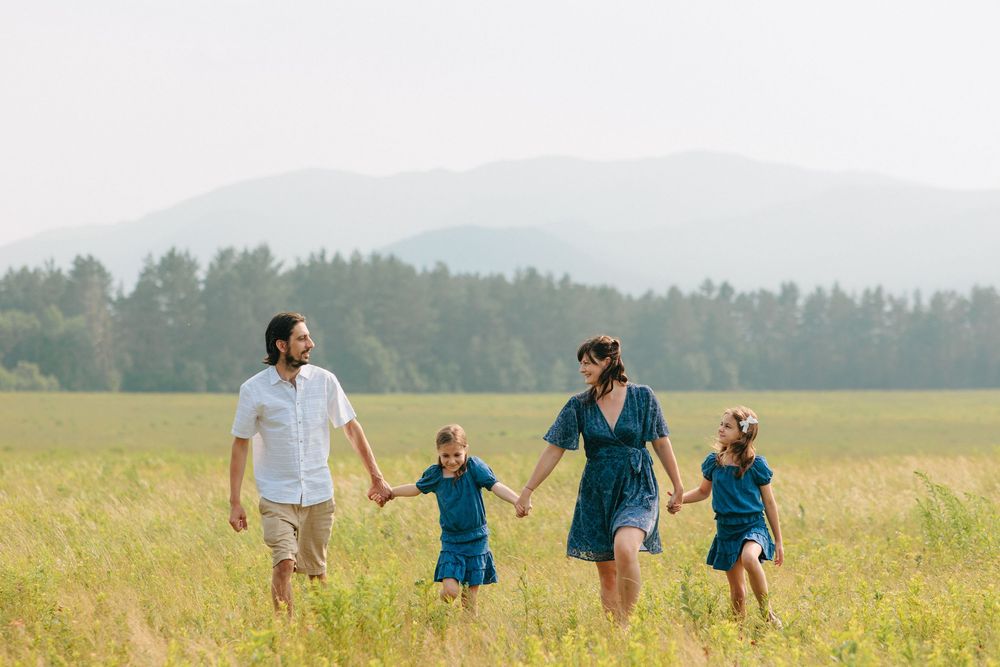 A family holds hands while running through a golden wheat field on a sunny summer day.