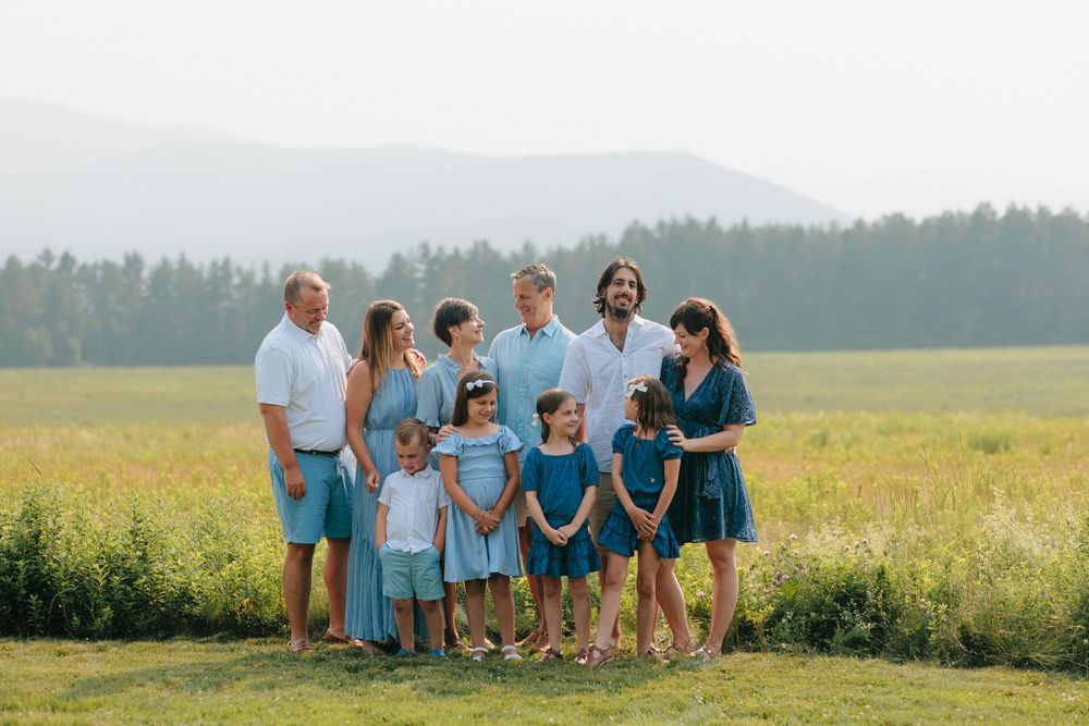 Family group in coordinated blue and white outfits walking together through a sunny meadow with mountains in background.