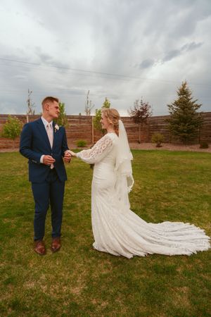 A bride and groom share a playful moment in a grassy field with a long flowing wedding dress trailing behind them.