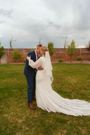 A romantic wedding couple embraces on a lawn with a wooden fence and stormy sky in the background.