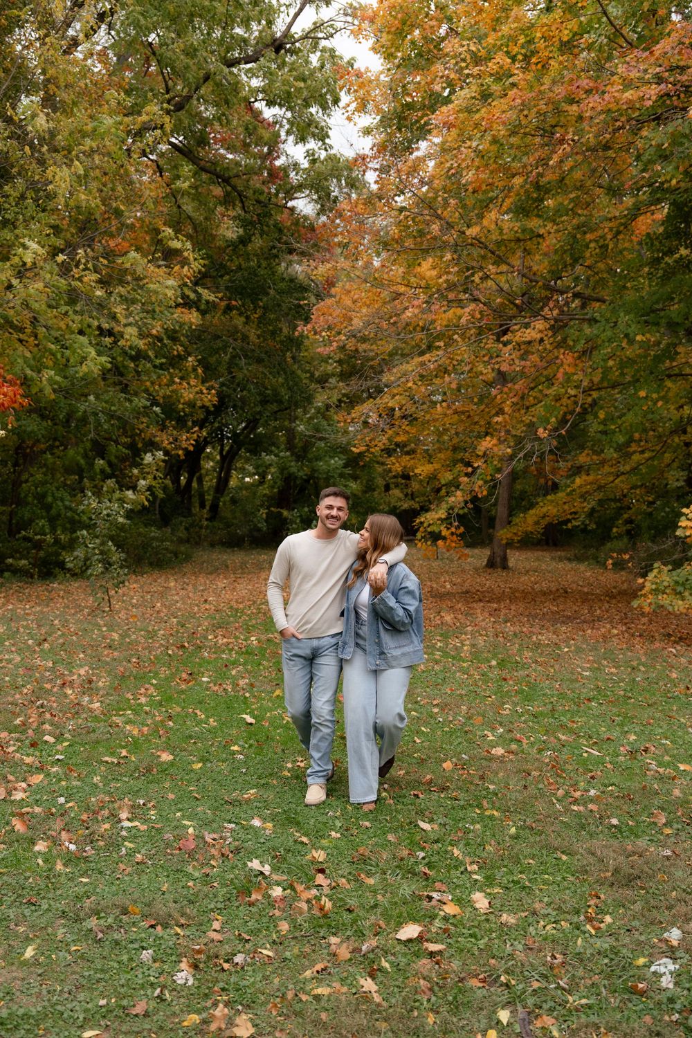 Couple walking together through a scenic autumn park with fallen leaves on the ground.