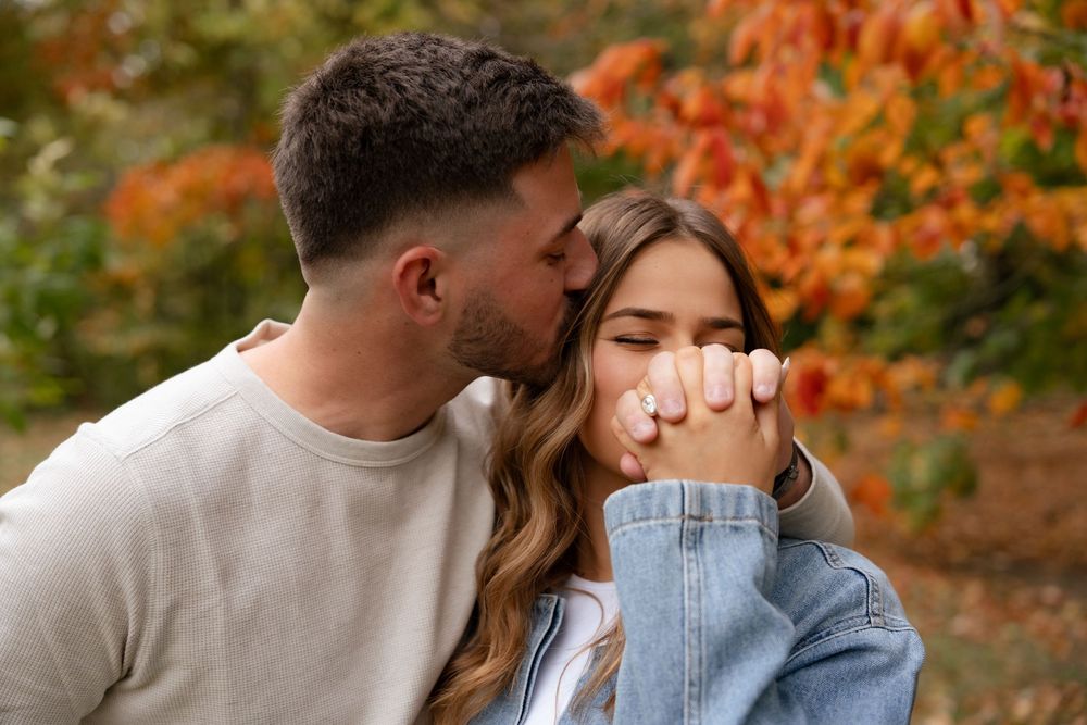 Romantic couple embraces under vibrant orange autumn foliage in an outdoor park setting.