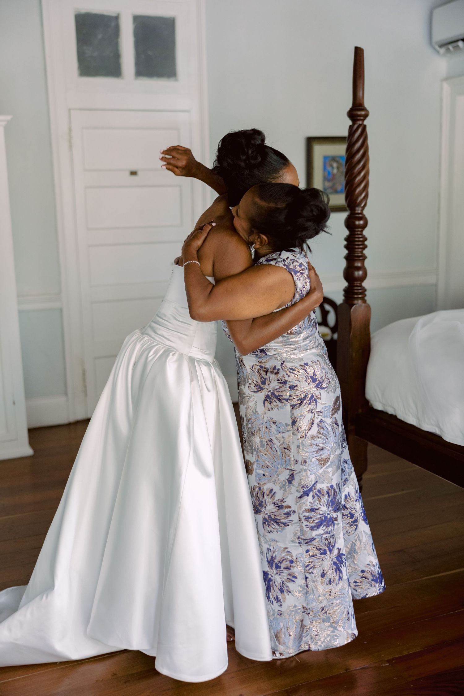 An intimate embrace between two people in formal attire featuring a white wedding dress and floral patterned dress.