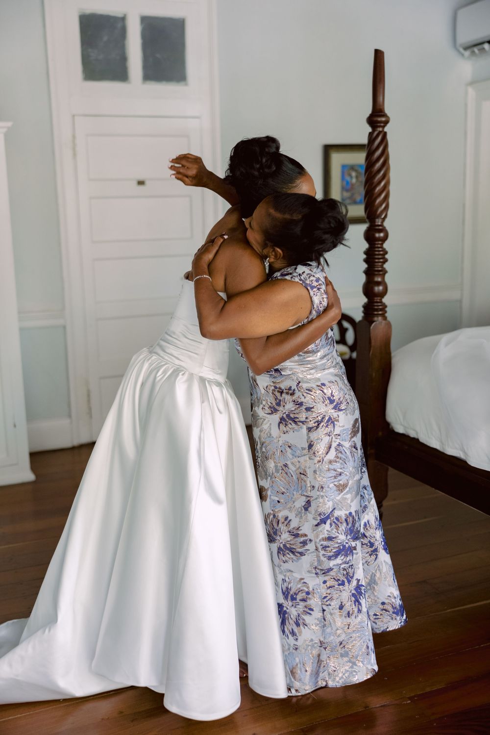 An intimate embrace between two people in formal attire featuring a white wedding dress and floral patterned dress.