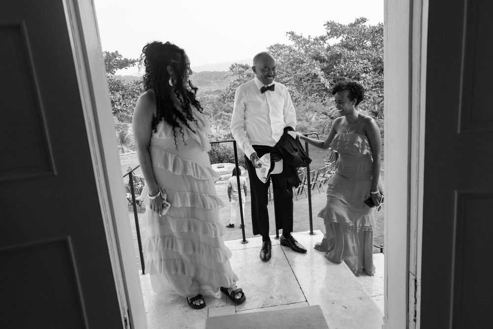 Black and white photo showing three people conversing at a doorway entrance, framed by the doorway perspective.