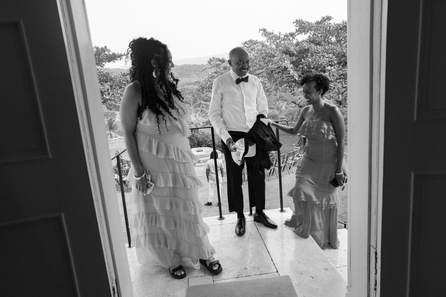 Black and white photo showing three people conversing at a doorway entrance, framed by the doorway perspective.
