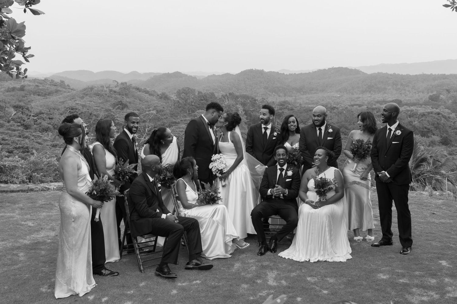 Group gathers on a scenic hillside for an outdoor wedding ceremony with mountain views in the background.
