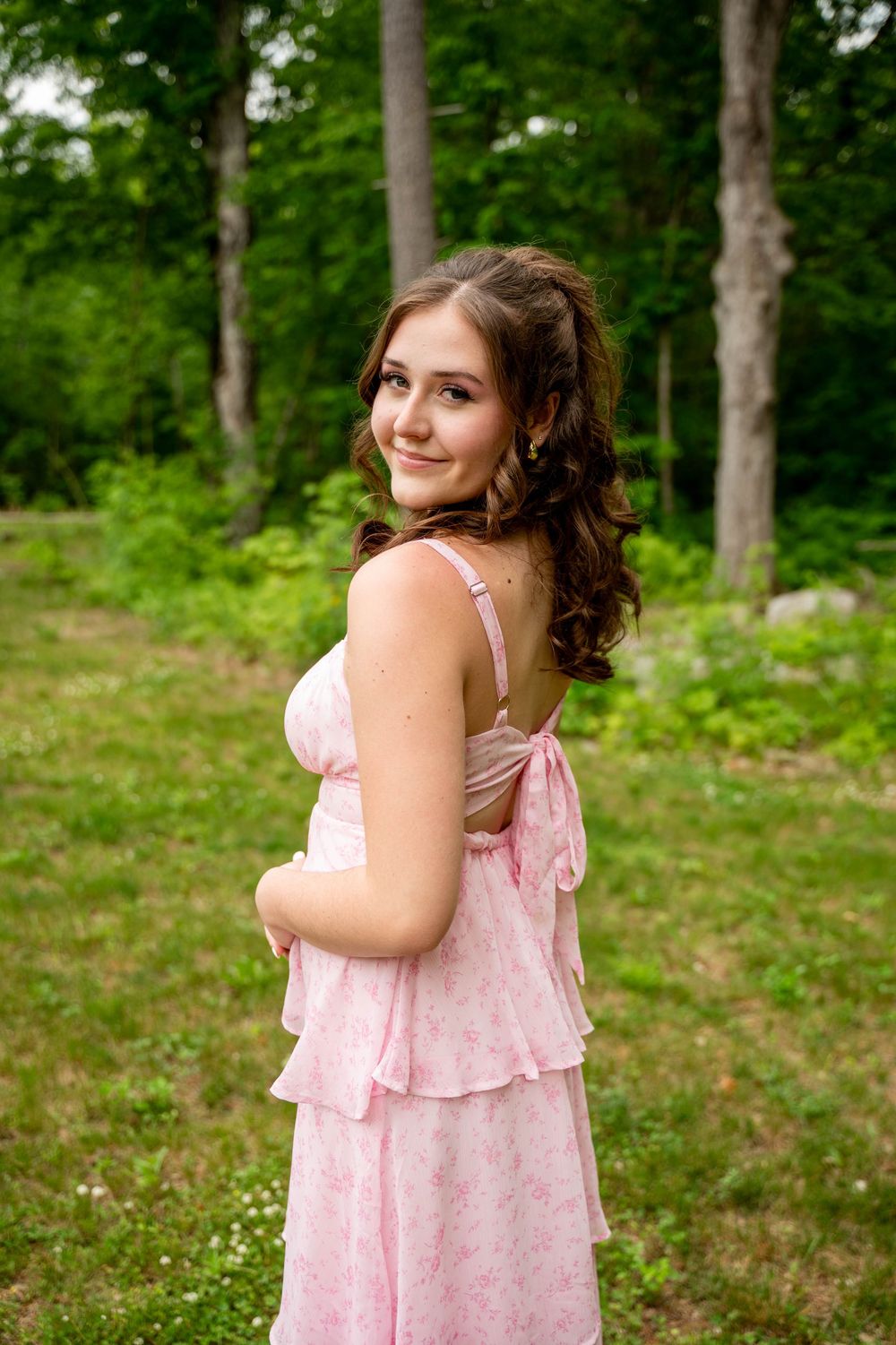 A person wearing a pink floral summer dress poses playfully in a lush green forest setting.