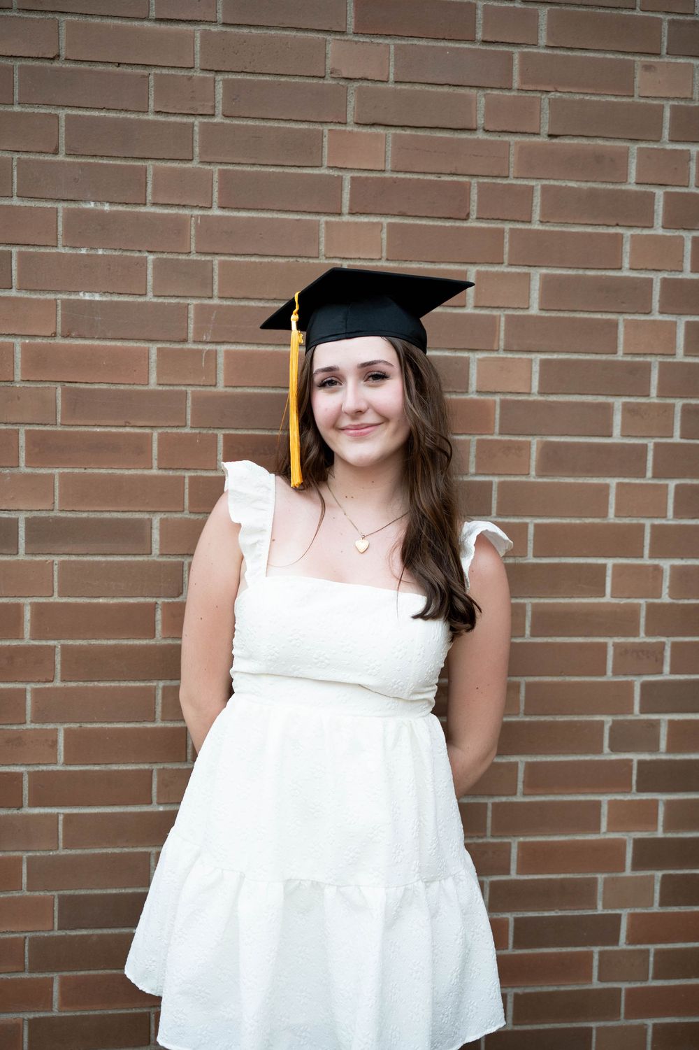 Graduate portrait showing smiling students wearing caps and gowns against a brick wall.
