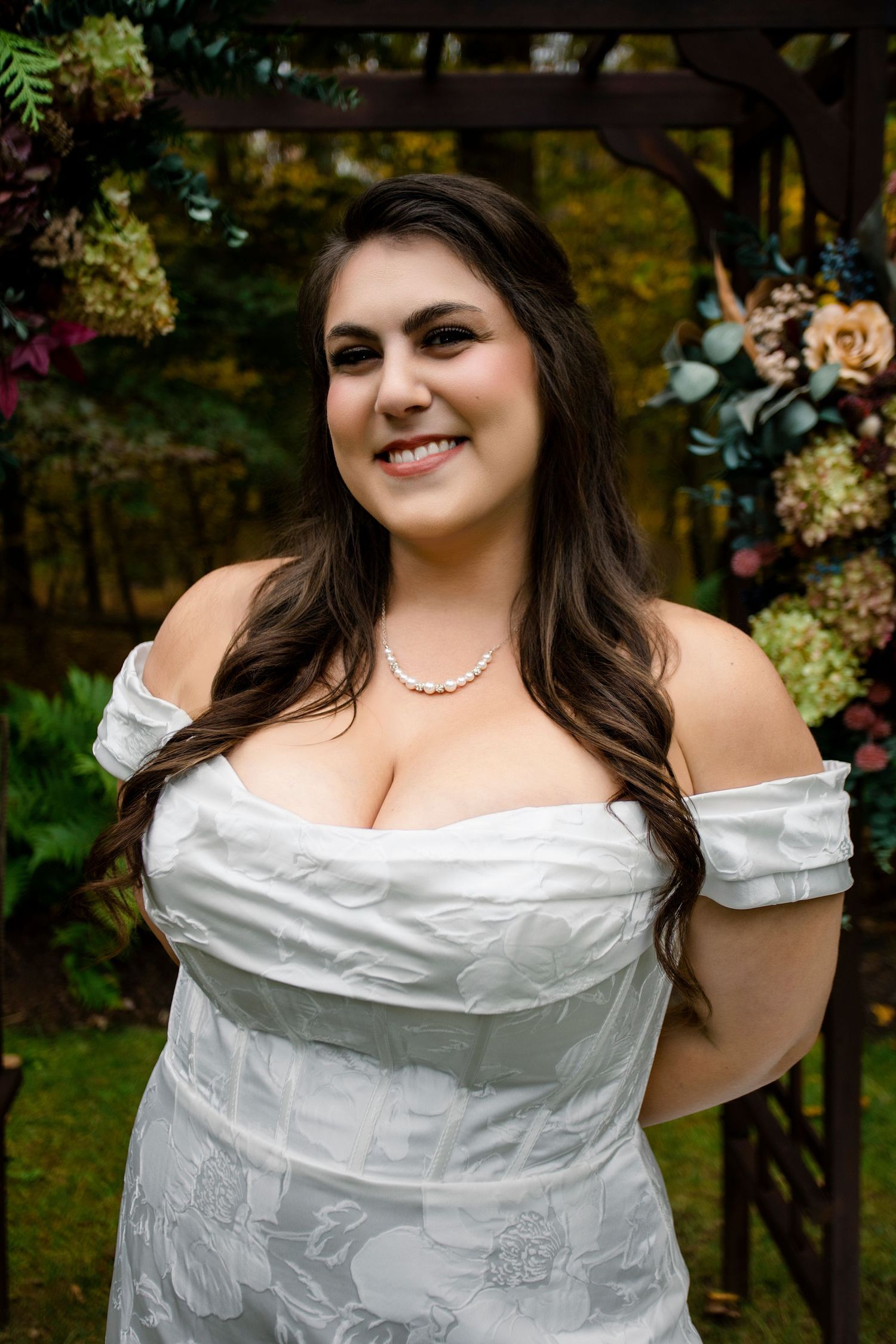 Bridal portraits in an off-shoulder white gown with pearl necklace in a garden setting.