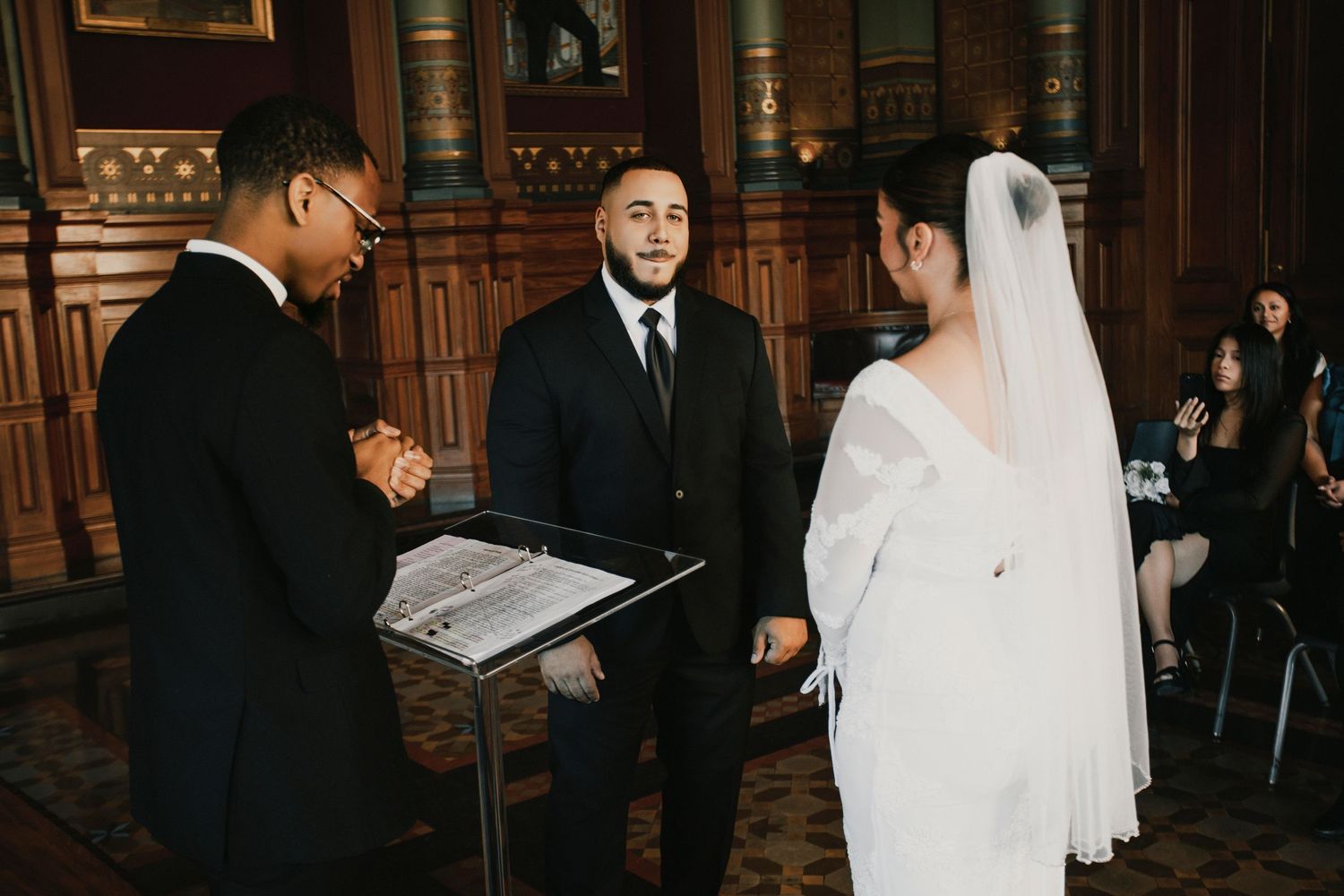 Indoor wedding ceremony in elegant wood-paneled room with guests seated.