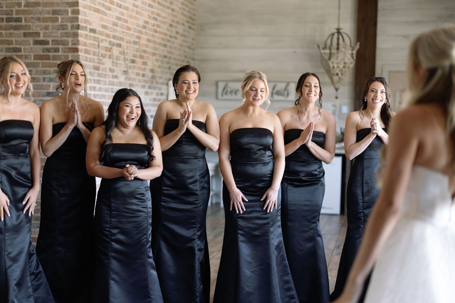 Bridesmaids in matching strapless navy blue satin gowns react with joy while viewing the bride.