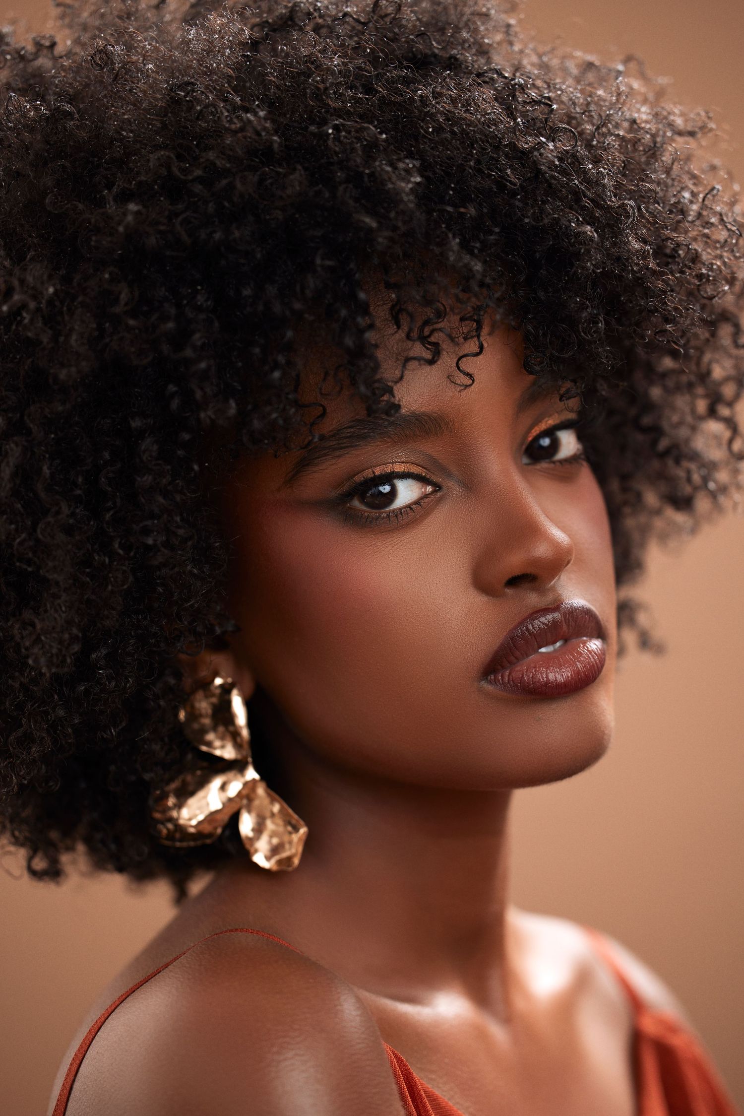 Close-up beauty shot showcasing natural curly hair and gold statement earrings.