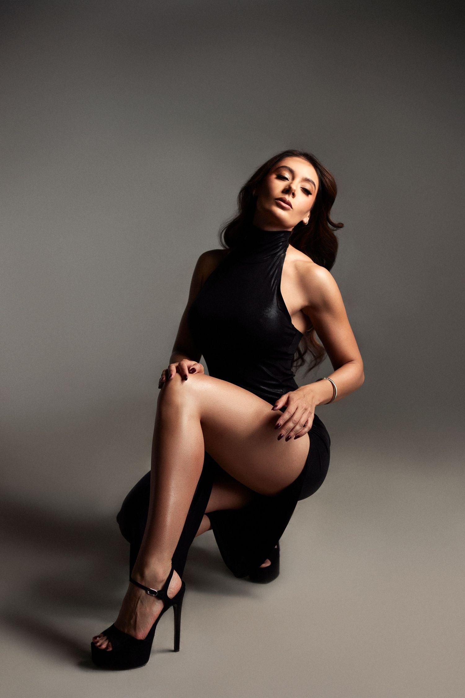 Moody studio portrait featuring black dress and high heels with dramatic shadows.